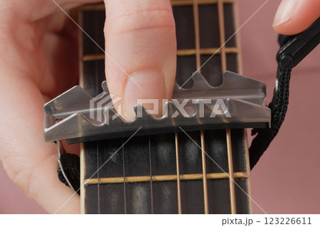 Extreme closeup view of woman's fingers as she attaches capodastro to guitar neck Extreme closeup view of woman's fingers as she attaches capodastro to guitar neck 123226611