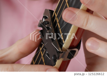 Female fingers attaches capotasto to Spanish six string acoustic guitar. Selective focus, handheld 123226612