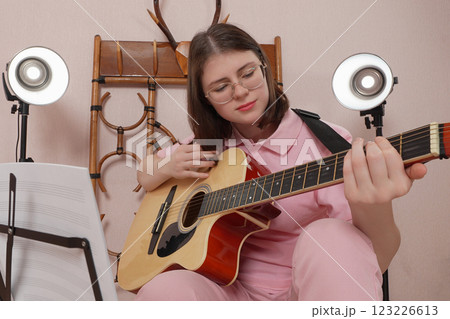 Young woman guitarist in eyeglasses practices strumming technique on acoustic classical guitar 123226613