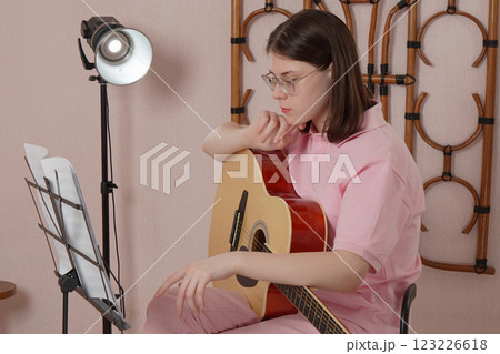 Woman with guitar sets up sheet music on music stand before playing acoustic guitar in home studio Woman with guitar sets up sheet music on music stand before playing acoustic guitar in home studio 123226618