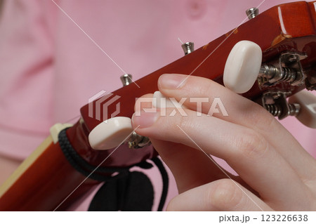 Extreme close-up of female fingers tuning acoustic guitar, tightening and loosening strings 123226638