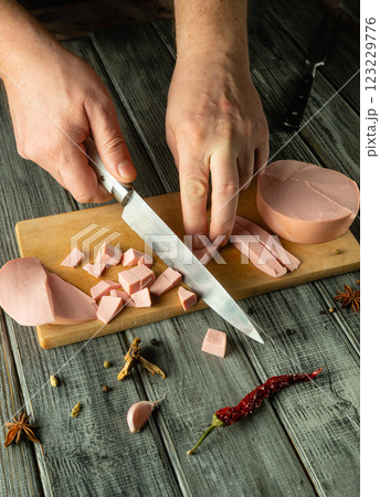 Hands skillfully chop slices of deli meat on a wooden board, surrounded by vibrant spices and herbs. The warm ambiance of the rustic kitchen adds to the culinary creativity 123229776