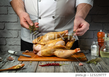 A skilled chef prepares a whole chicken for cooking, carefully adding fresh herbs and spices. The rustic kitchen setting enhances the culinary atmosphere, perfect for a delicious meal A skilled chef prepares a whole chicken for cooking, carefully adding fresh herbs and spices. The rustic kitchen setting enhances the culinary atmosphere, perfect for a delicious meal 123229777
