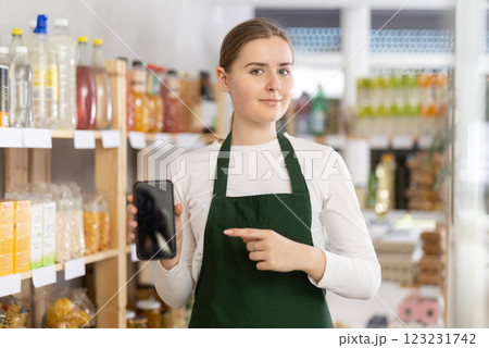 Female seller in uniform showing information on smartphone screen in store Female seller in uniform showing information on smartphone screen in store 123231742