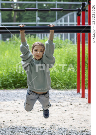 Young girl practicing on horizontal bars outdoors in recreational park area Young girl practicing on horizontal bars outdoors in recreational park area 123233526