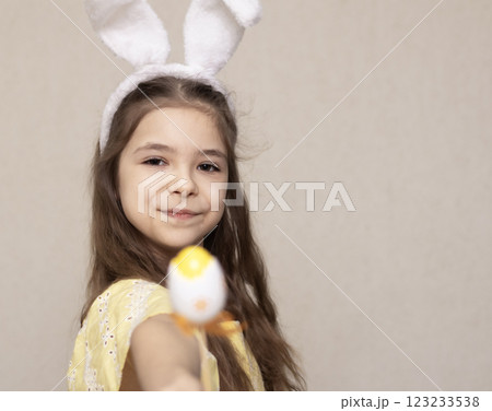 Smiling girl wearing bunny ears holding Easter egg in bright yellow setting Smiling girl wearing bunny ears holding Easter egg in bright yellow setting 123233538
