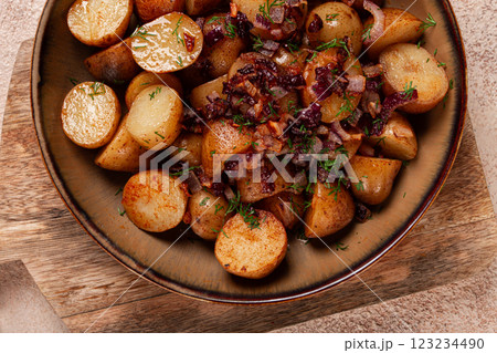 Delicious roasted potatoes garnished with caramelized onions and fresh herbs served in a rustic bowl 123234490