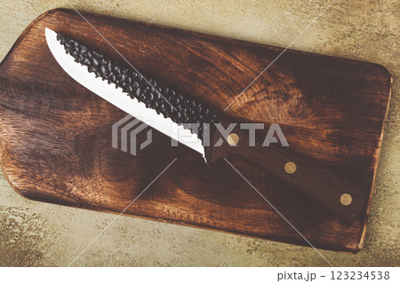 High-quality kitchen knife resting on a wooden cutting board with intricate textures and a rustic design 123234538