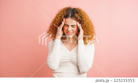 Young woman suffering from strong headache touching temples on pink background 123235353