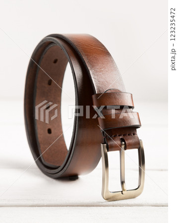Brown genuine leather belt on a white wooden background. Brown genuine leather belt on a white wooden background. 123235472