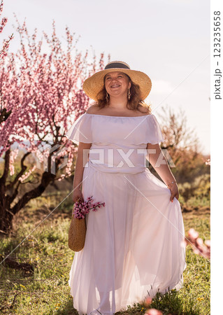 Woman blooming peach orchard. Against the backdrop of a picturesque peach orchard, a woman in a long white dress and hat enjoys a peaceful walk in the park, surrounded by the beauty of nature. Woman blooming peach orchard. Against the backdrop of a picturesque peach orchard, a woman in a long white dress and hat enjoys a peaceful walk in the park, surrounded by the beauty of nature. 123235658