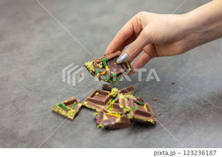Woman's hand holds piece of Dubai chocolate on gray background. Green kadayif and pistachio spread with pistachio in trend dessert. Close-up, selective focus. High quality photo Woman's hand holds piece of Dubai chocolate on gray background. Green kadayif and pistachio spread with pistachio in trend dessert. Close-up, selective focus. High quality photo 123236187