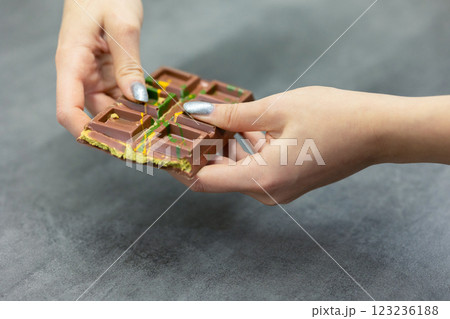 Female hands breaking off piece of Dubai chocolate on gray background. Green kadayif and pistachio spread with pistachio in trend dessert. Close-up, selective focus. High quality photo 123236188