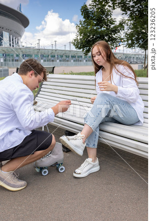 Man helps to tie laces on quad rollers. Young couple rollerblading in park. Vertical photo. High quality photo Man helps to tie laces on quad rollers. Young couple rollerblading in park. Vertical photo. High quality photo 123236205
