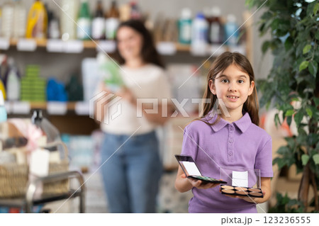 Little girl longingly looks at eye shadow pallet in shop and dreams of makeup like adult lady 123236555