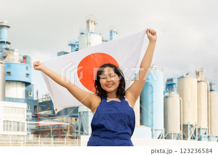 Happy young woman with flag of Japan against background of factory 123236584