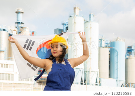 Happy asian girl in work clothes and hardhat with flag of south korea standing in front of industrial scenery 123236588