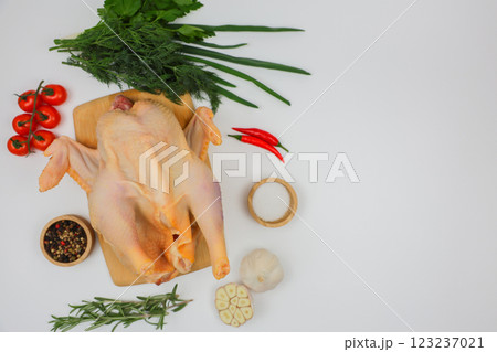 A raw processed chicken carcass lies on a wooden board with spices in wooden bowls, herbs, herbs and vegetables with space for text on a white background. The concept of cooking, wholesome and healthy 123237021