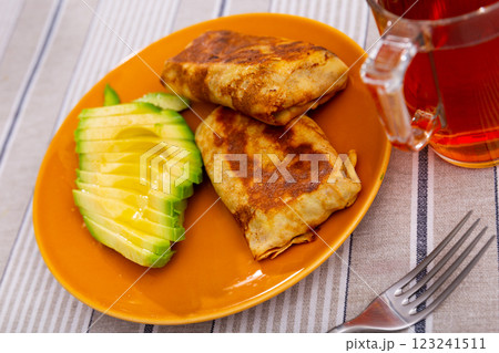 There are pancakes with liver and egg filling on plate, supplemented with half chopped avocado 123241511