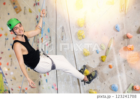 Determined young man in safety helmet doing his best at climbing artificial wall 123241708
