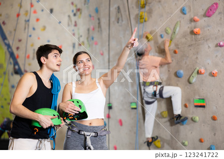 Happy excited young male and female visitors discussing upcoming climbing artificial training rock wall in indoor bouldering gym 123241722