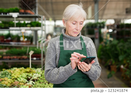 Elderly woman plant shop worker using smartphone Elderly woman plant shop worker using smartphone 123241874