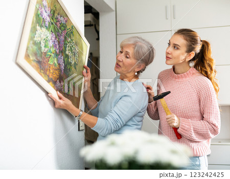 Senior woman and granddaughter trying to put picture on wall 123242425