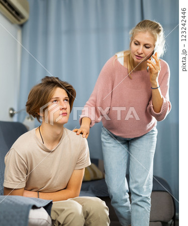 Teenager suffering from stomach pain while mother speaking on phone 123242446