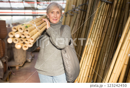 Senior woman carrying bunch of bamboo poles in home goods store Senior woman carrying bunch of bamboo poles in home goods store 123242450
