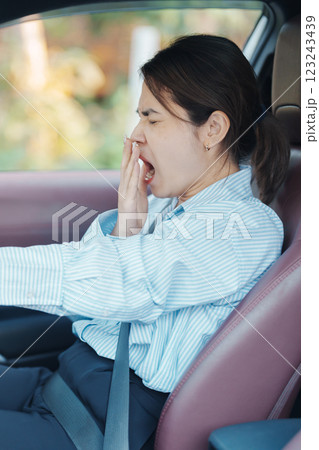 woman feeling sleepy and yawn during drive car long time. Asian girl tired and fatigue having headache after driving car in traffic jam. Sleep, stretching and safety concept 123243439