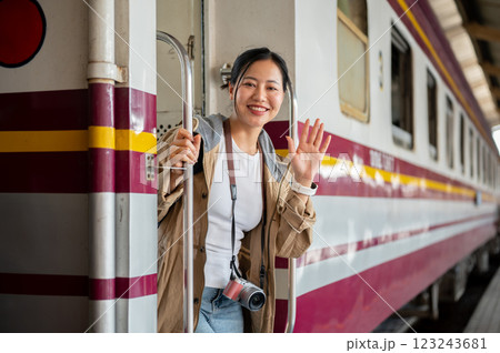 Smiling asian woman with camera is waving hand while coming down from carriage at train station 123243681