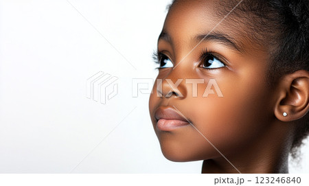 Young girl with a smooth complexion gazes upwards with striking eyes. She has an earring and is set against a solid white backdrop. 123246840
