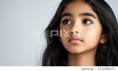 Serene portrait of a young girl with dark hair looking towards the upper left, showcasing her calm and reflective expression. 123246875