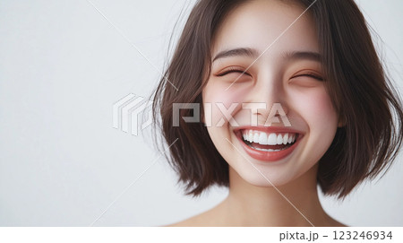 Radiant young woman smiles brightly, her eyes closed in joyful expression, showcasing happiness and youthful energy on a clean background. 123246934