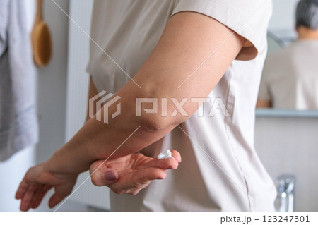 A mature woman of the pensioner age with dry skin smears moisturizing cream on her elbows. 123247301