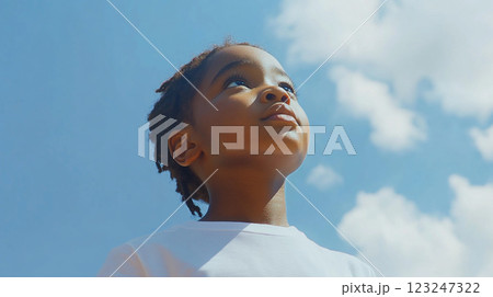A young child looks up at a vast blue sky dotted with fluffy white clouds, a hopeful and innocent gaze towards the heavens above. 123247322
