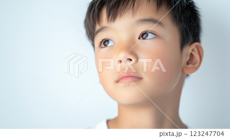 A close-up of a young boy with a thoughtful expression, looking upwards with soft lighting, isolated against a plain background. 123247704