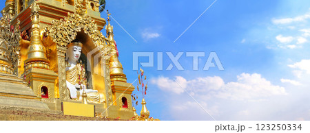 Horizontal banner with statue of Buddha in golden ancient buddhist stupa. Stone figure of Buddha near to buddhist temple, Yangon, Myanmar (Burma). On blue sky background. Copy space for text 123250334