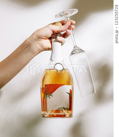 Hand holding a bottle of wine and a glass in a bright setting 123250728