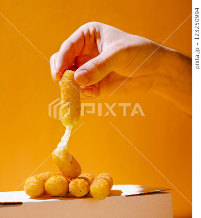 Hand reaching for cheesy snack against vibrant orange background 123250994