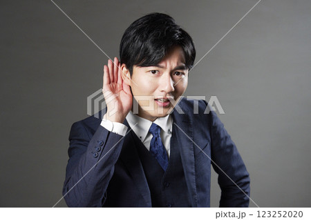 耳に手を当てるビジネスマン　黒背景 123252020