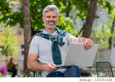 Middle-aged man opens laptop start working sends messages sitting on chair in urban city street 123252188