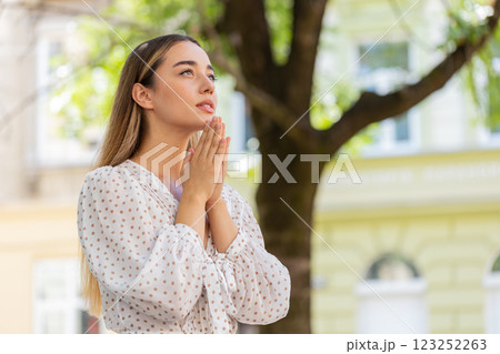 Caucasian young woman praying with closed eyes to god asking for blessing help forgiveness outdoors Caucasian young woman praying with closed eyes to god asking for blessing help forgiveness outdoors 123252263