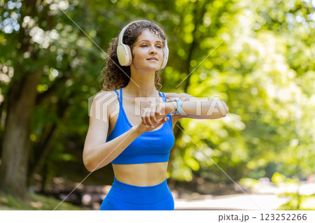 Athletic runner woman looks at smart watch device fitness bracelet checking time, heart rate, pulse 123252266