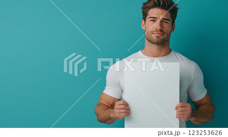 A handsome man with a warm expression holds a blank white board against a vibrant turquoise backdrop, inviting viewers to consider possibilities. 123253626