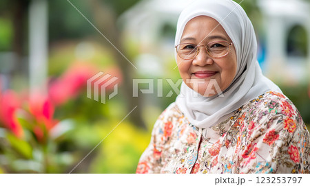 A smiling woman in a hijab, wearing glasses and a floral top, exudes warmth and grace in a garden setting. Her serene presence is captivating. A smiling woman in a hijab, wearing glasses and a floral top, exudes warmth and grace in a garden setting. Her serene presence is captivating. 123253797