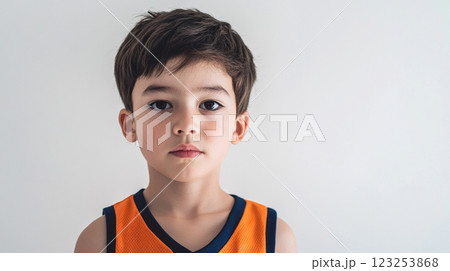 Portrait of a young boy with brown hair and eyes, wearing a sports jersey against a plain white background. Neutral expression on his face. 123253868
