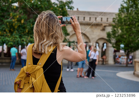 Female tourist with yellow backpack taking photo of historic landmark in Budapest during travel. Woman using smartphone to capture travel and sightseen moments in European city 123253896