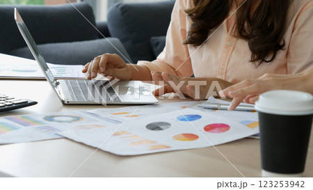 Asian Female freelance using laptop at home office desk. Woman reading financial graph chart Planning analyzing marketing data. Asian female people working office firm with business stuff, coffee cup 123253942