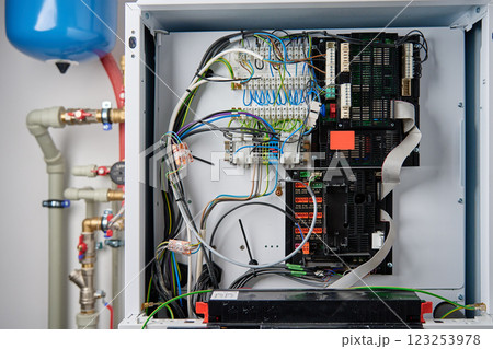 Close-up of boiler control panel with exposed electrical wiring, circuit board, and terminal connections. Modern heating system with complex electronic components Close-up of boiler control panel with exposed electrical wiring, circuit board, and terminal connections. Modern heating system with complex electronic components 123253978